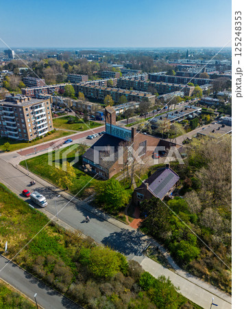 Aerial view of a residential neighborhood with a church at the center, surrounded by apartment buildings, green spaces, roads, and trees under a clear sky. Aerial view of a residential neighborhood with a church at the center, surrounded by apartment buildings, green spaces, roads, and trees under a clear sky. 125248353