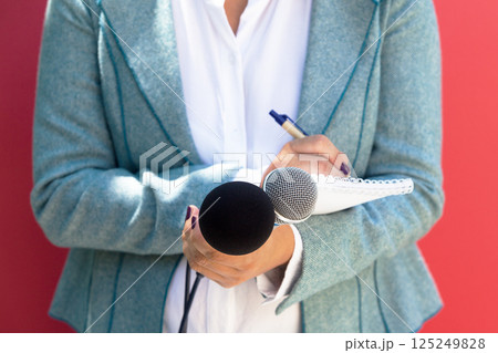 Female journalist at news conference, writing notes, holding microphone 125249828