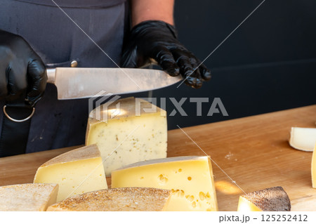 A vendor slices a piece of cheese with a knife at a farmers market 125252412