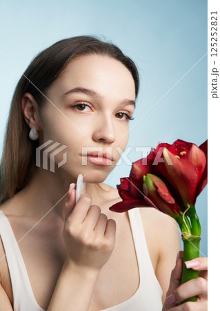 Woman applying skincare while holding red flowers in a serene setting Woman applying skincare while holding red flowers in a serene setting 125252821