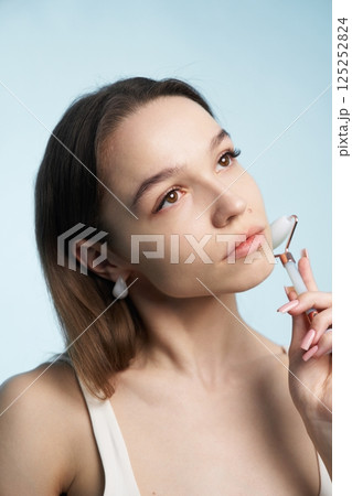 Woman using facial roller while contemplating beauty routine in soft lighting Woman using facial roller while contemplating beauty routine in soft lighting 125252824