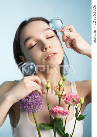 Woman holding glass spheres and flowers in a serene studio setting Woman holding glass spheres and flowers in a serene studio setting 125252826
