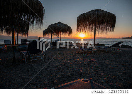A beach with umbrellas and chairs and a sunset in the background 125255151
