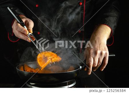 A chef maneuvers tongs to expertly flip golden pumpkin slices sizzling in a frying pan. Wisps of steam curl upwards, showcasing a vibrant culinary environment filled with flavors A chef maneuvers tongs to expertly flip golden pumpkin slices sizzling in a frying pan. Wisps of steam curl upwards, showcasing a vibrant culinary environment filled with flavors 125256384
