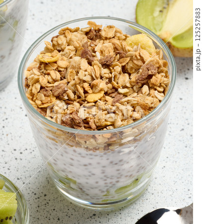 Glass filled with chia seed pudding, layered with diced kiwi at the bottom and topped with crunchy granola 125257883