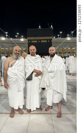 Three Muslim men in Ihram clothing standing in front of the Kaaba during Hajj or Umrah pilgrimage in Mecca, Saudi Arabia. Sacred Islamic journey at Masjid al-Haram 125258693