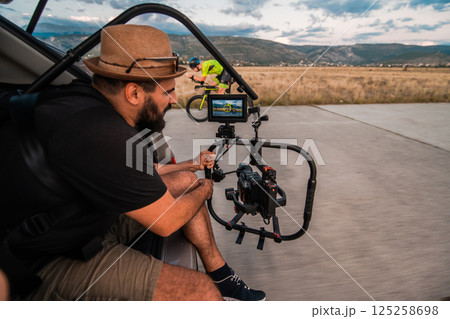 A videographer recording a triathlete riding his bike preparing for an upcoming marathon.Athlete's physical endurance and the dedication required to succeed in the sport. A videographer recording a triathlete riding his bike preparing for an upcoming marathon.Athlete's physical endurance and the dedication required to succeed in the sport. 125258698
