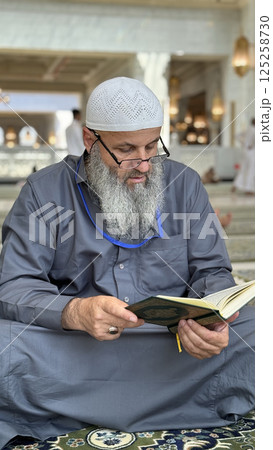 Mecca, Saudi Arabia - May 2, 2024: Young man, Hajj and Umrah pilgrim sitting and reading Quran in Masjidil Haram, Great Mosque in Makkah, Saudi Arabia. Hajj 2024. 125258730