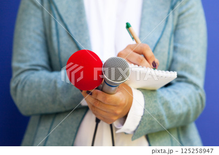 Journalist at press conference, taking notes, holding microphone 125258947