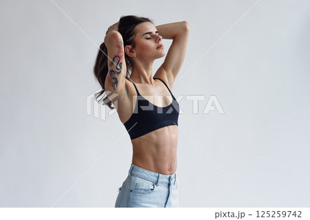 Charming skinny beautiful girl with perfect abs in jeans and black top isolated on light background Charming skinny beautiful girl with perfect abs in jeans and black top isolated on light background 125259742