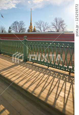 View on the Peter and Paul Fortress spire through iron railings at sunset 125259772