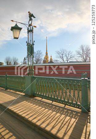 View on the Peter and Paul Fortress spire through iron railings at sunset 125259773