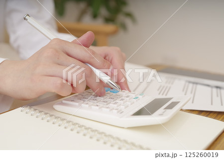 電卓で計算をする女性の手元 125260019