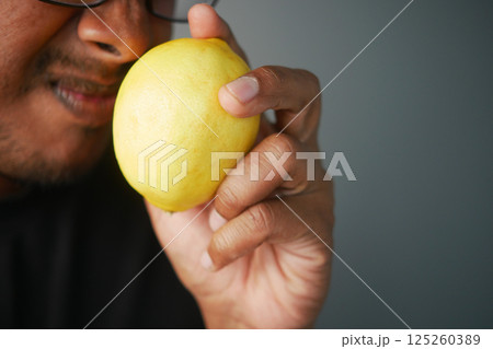 Man examining a yellow lemon in a close-up setting indoors Man examining a yellow lemon in a close-up setting indoors 125260389