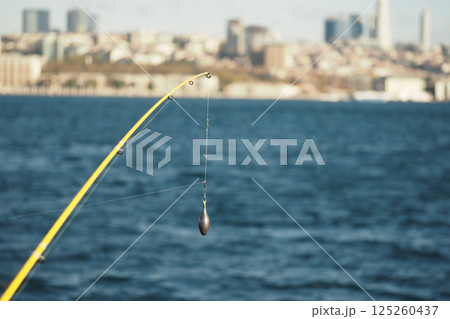 Fishing line casts over calm water with city skyline in background Fishing line casts over calm water with city skyline in background 125260437