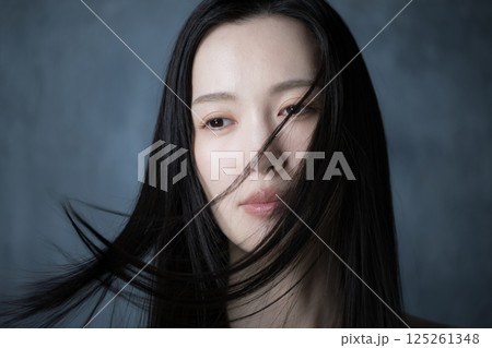 グレーバックで髪をなびかせる美容やビューティーのイメージの女性のクローズアップ 125261348