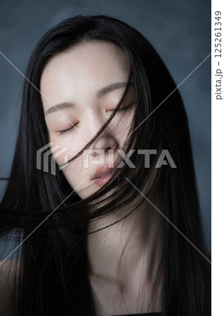 グレーバックで髪がなびく美容やビューティー、決意や意志の強さがカッコイイ真剣な表情の目を閉じる女性 125261349