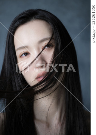 グレーバックで髪がなびく美容やビューティー、決意や意志の強さがカッコイイ真剣な表情の女性のクローズ 125261350