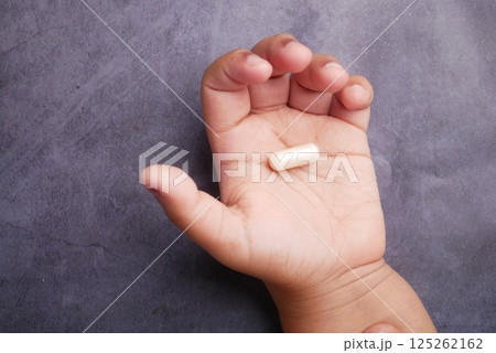 Child's hand holding a dietary supplement capsule in natural light 125262162