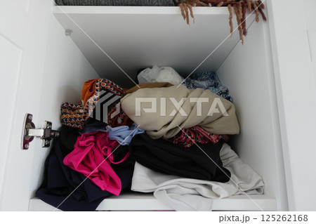 Clothes are disorganized in a cluttered closet shelf 125262168