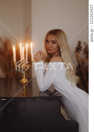 Elegant woman in white dress leaning on black piano. Loft interior. Elegant woman in white dress leaning on black piano. Loft interior. 125263427