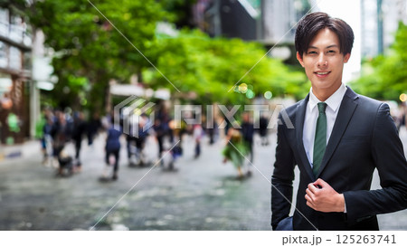 スーツ姿の若い男性が緑の街並みにたたずみ爽やかな笑顔を見せるポートレート スーツ姿の若い男性が緑の街並みにたたずみ爽やかな笑顔を見せるポートレート 125263741