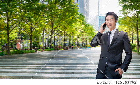 スーツ姿の若い男性が電話をする、都会の並木道で笑顔を見せるビジネスパーソン 125263762