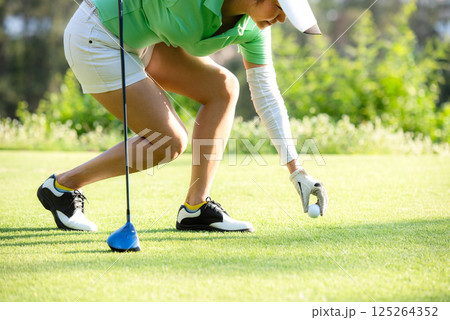 Asia sporty woman put golf ball on tee with club in golf course Asia sporty woman put golf ball on tee with club in golf course 125264352