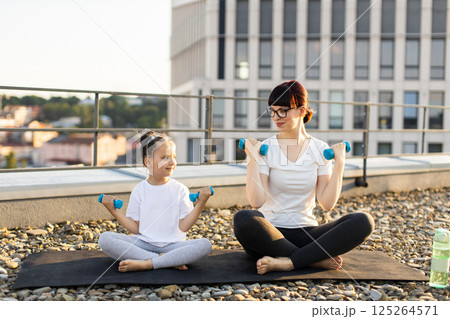 Mother and daughter, adult female and young girl, practicing fitness with dumbbells on rooftop Mother and daughter, adult female and young girl, practicing fitness with dumbbells on rooftop 125264571