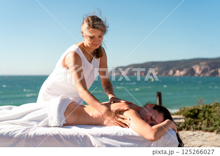 Masseur giving back massage to woman near sea at 125266027