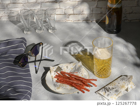 Still life with a glass of beer, fish straws, sunglasses and a vest, casting shadows from the sun Still life with a glass of beer, fish straws, sunglasses and a vest, casting shadows from the sun 125267778