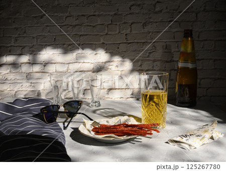 Still life with a glass of beer, fish straws, sunglasses and a vest, casting shadows from the sun 125267780
