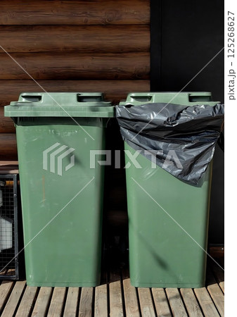 green trash cans positioned on wooden deck near rustic wall without any litter or debris in sight. 125268627