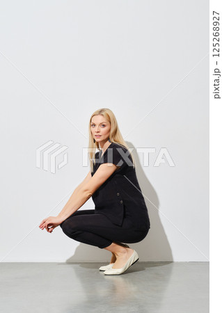 Woman squatting in profile next to a white wall Woman squatting in profile next to a white wall 125268927