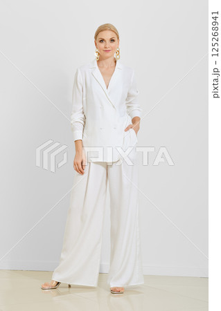 Elegant woman wearing a loose white outfit poses confidently against a neutral backdrop 125268941