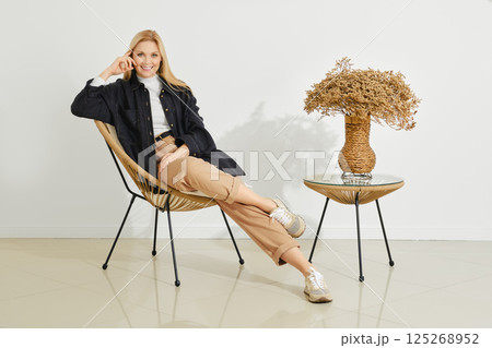 Woman sitting in a modern chair with a decorative plant beside her in a minimalist setting Woman sitting in a modern chair with a decorative plant beside her in a minimalist setting 125268952