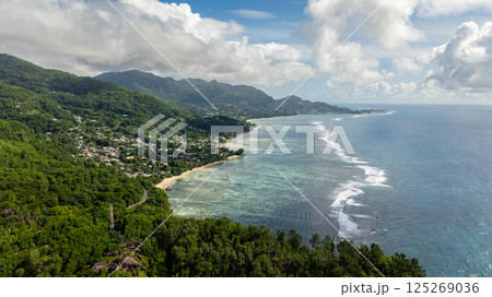Turquoise ocean water bordered by a dense forest shoreline, crystal clear with coral reefs. Seychelles, Mahe. 125269036