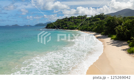 Tropical waves crashing onto a sandy beach, surrounded by dense green vegetation. Anse Louis. Seychelles, Mahe. Tropical waves crashing onto a sandy beach, surrounded by dense green vegetation. Anse Louis. Seychelles, Mahe. 125269042