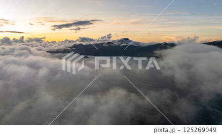 A golden sky with dramatic clouds shines above the mist-covered ocean as the sun begins to rise. Seychelles, Mahe. 125269049
