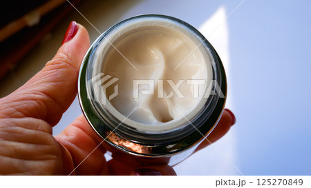 Open jar of face cream in a woman's hand. 125270849