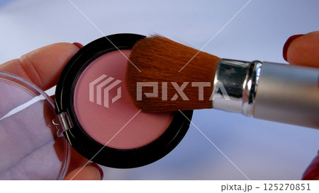 The brush touches and picks up pink face makeup blush from an open box. 125270851