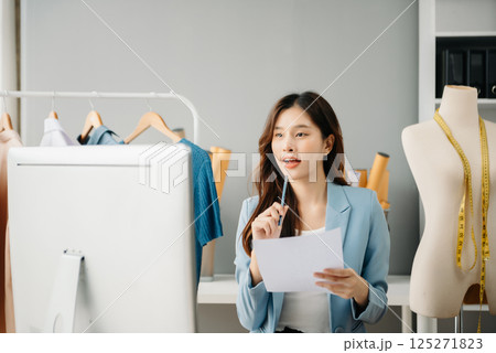 Asian young woman on desk in office of fashion designer and holds tablet, laptop and smartphone Asian young woman on desk in office of fashion designer and holds tablet, laptop and smartphone 125271823