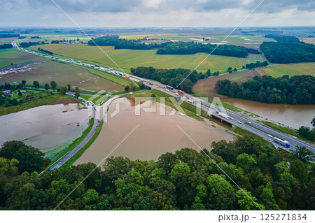 Aerial view of flooded fields and submerged rural road near busy highway. Concept of climate impact, transportation disruption and natural disaster Aerial view of flooded fields and submerged rural road near busy highway. Concept of climate impact, transportation disruption and natural disaster 125271834