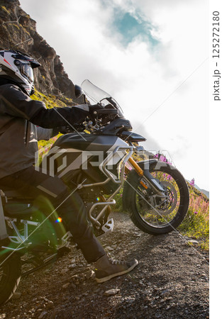 Motorcycle rider riding in Italian Alps during sunrise, dramatic sky. Travel and freedom, outdoor activities 125272180