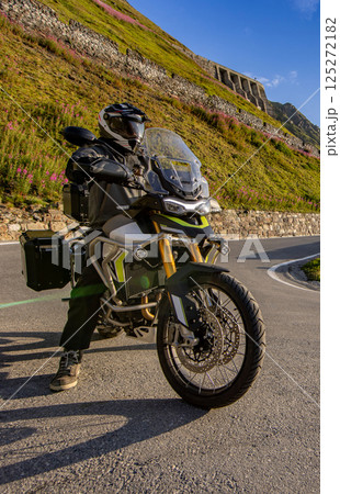 Motorcycle rider riding in Italian Alps during sunrise, dramatic sky. Travel and freedom, outdoor activities 125272182