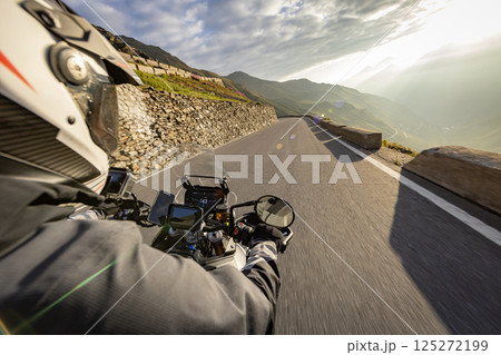 Motorcycle rider riding in Italian Alps during sunrise , handlebar view , dramatic sky . Travel and freedom, outdoor activities 125272199