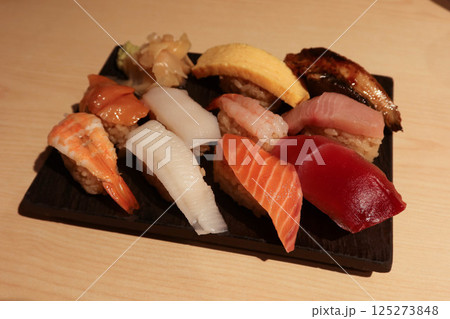 Close up of ten Japanese sushi on a wooden serving board, including salmon, prawn, squid, tuna, scallop, egg, eel and flounder. Ginger slice  and wasabi on the side.  125273848
