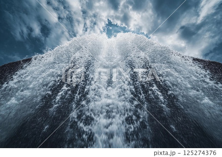 Powerful waterfall cascading from rocky cliffs under a bright blue sky Powerful waterfall cascading from rocky cliffs under a bright blue sky 125274376