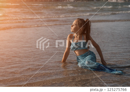 A girl in a mermaid costume on the beach. Sunset on the shore of the blue sea. Childhood happiness, beach, vacation, sunscreen, warm weather, travel. High quality photo A girl in a mermaid costume on the beach. Sunset on the shore of the blue sea. Childhood happiness, beach, vacation, sunscreen, warm weather, travel. High quality photo 125275766
