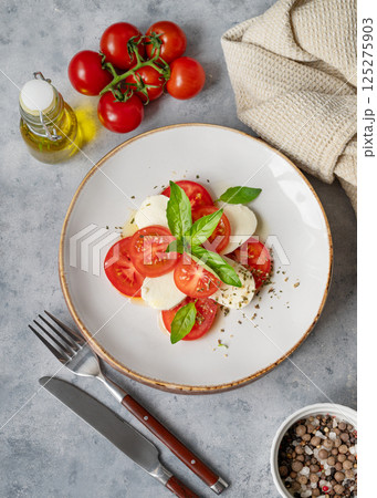 Caprese salad with sliced tomatoes, mozzarella and basil on a plate on a light background 125275903
